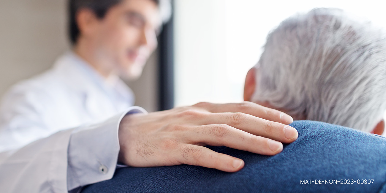 Arzt hält seine rechte Hand auf die Schulter eines älteren Mannes